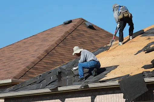 Roofers removing old asphalt shingles from the roof